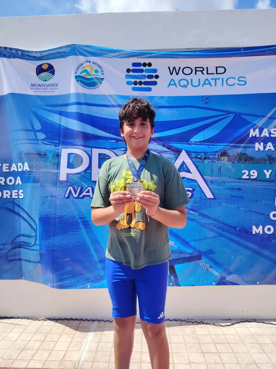 Niño sonriente muestra su medalla de una competencia de natación frente a la lona de PROA Nadadores